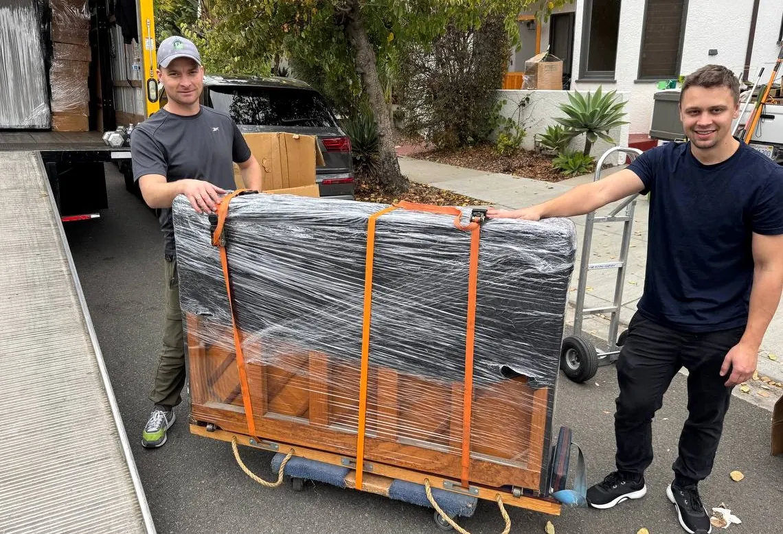 LA Moving crew handling a wrapped piano beside their moving truck